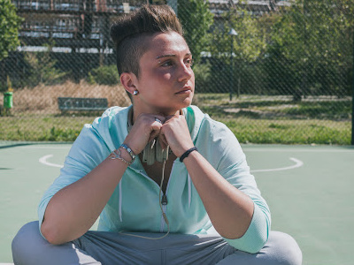 Trans man sitting on tennis court in sweatshirt and sweatpants