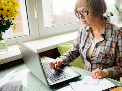 Woman looking at laptop with papers beside her