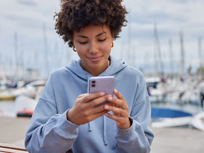Black young woman looking at cell phone while by a dock with boats 