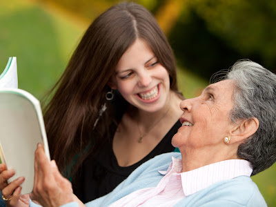 Young woman smiling with grandmother while looking at a book outside 
