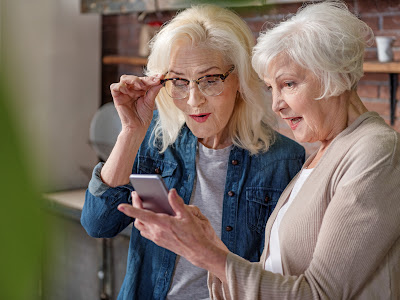 Two older women with white hair having trouble seeing cell phone with glasses